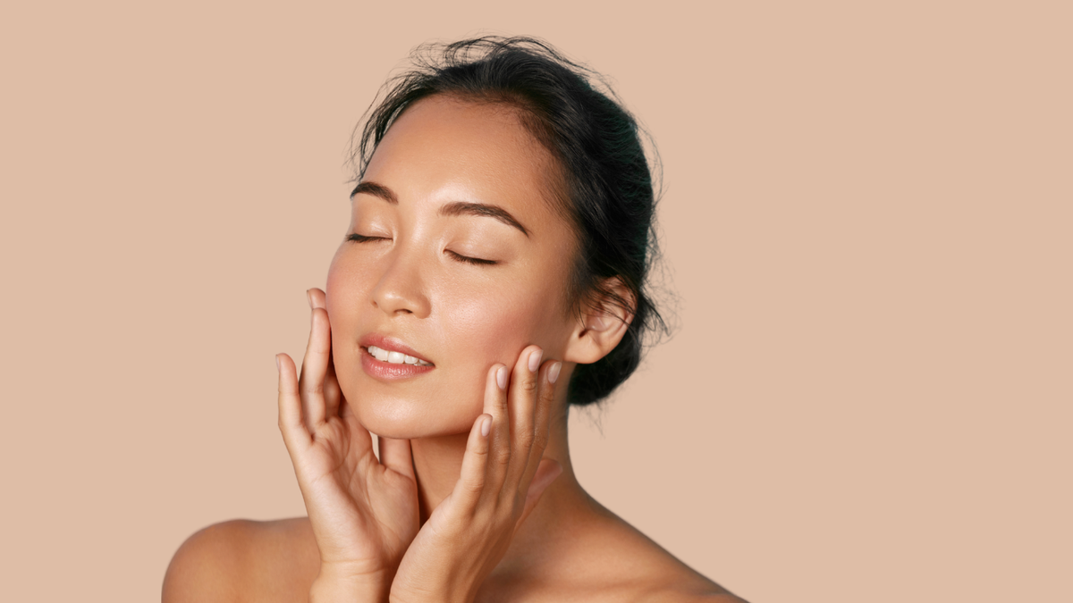 A smiling woman resting her chin on her hands beside CUMA turmeric skincare