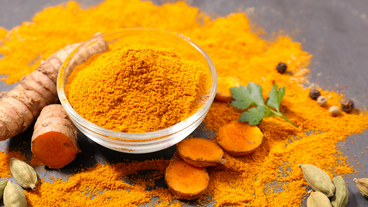 Turmeric powder in a wooden bowl beside fresh turmeric roots