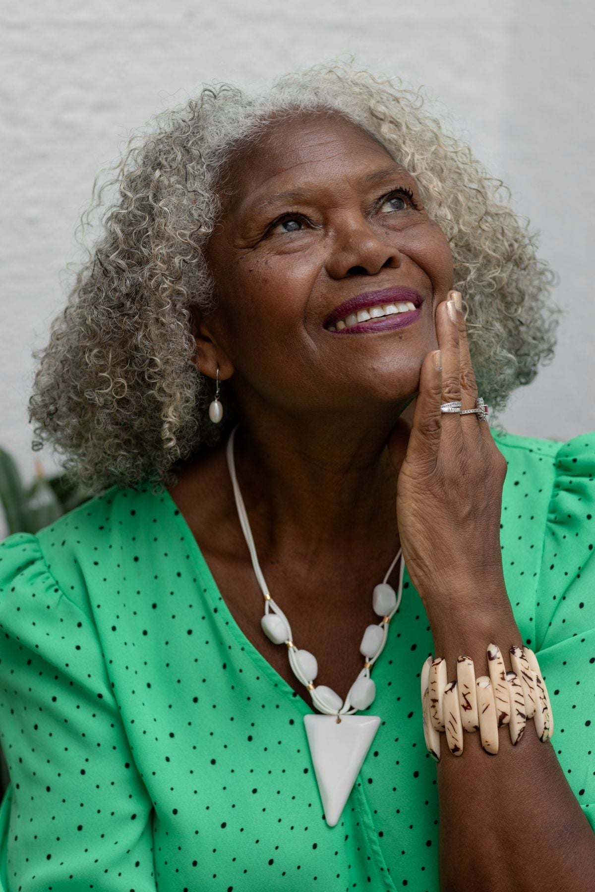 A silver-haired African-American woman smiling with her hand resting softly on her cheek