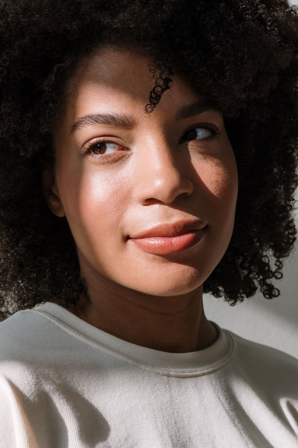 A young African-American woman with naturally curly hair and glowing skin in soft window light