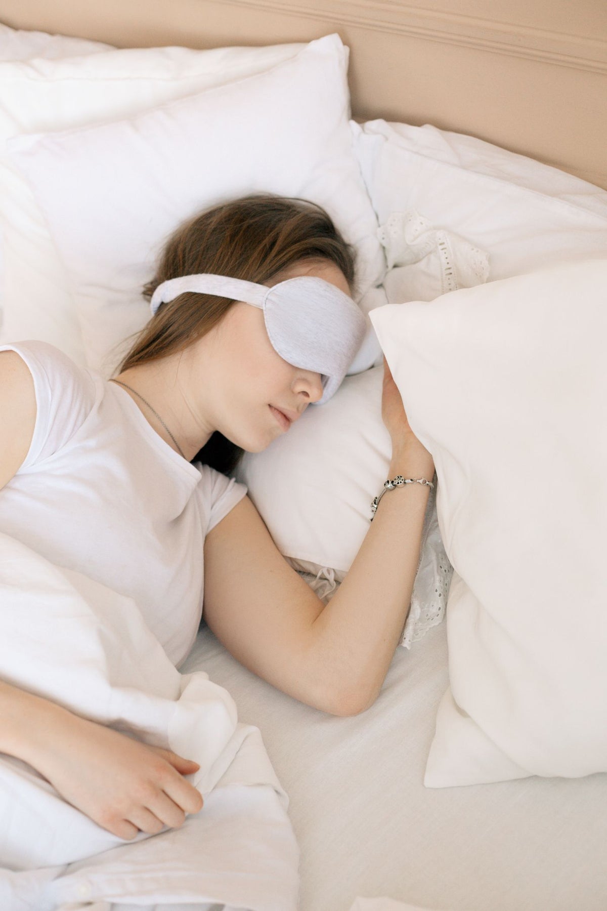 A woman sleeping peacefully on white linen with a silk eye mask