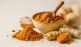 Turmeric powder in a wooden bowl beside fresh turmeric roots